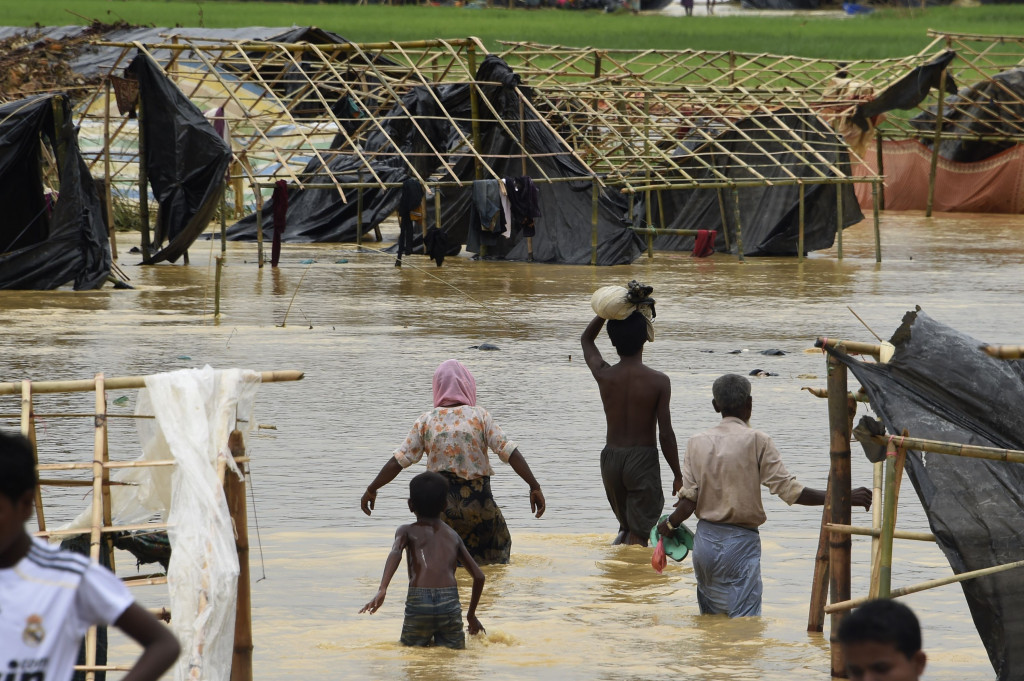 Beberapa pengungsi Rohingya menyeberangi genangan banjir di Thyangkali, Ukhia, Bangladesh. Hujan lebat juga merusak tenda-tenda pengungsian yang belum lama didirikan.