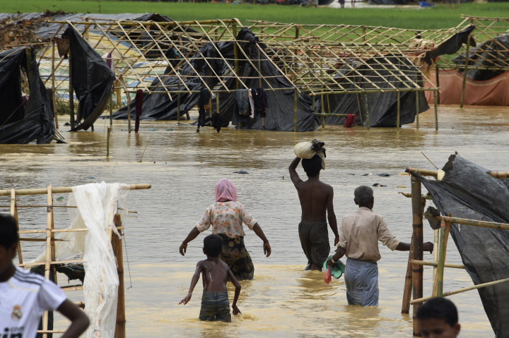 Beberapa pengungsi Rohingya menyeberangi genangan banjir di Thyangkali, Ukhia, Bangladesh. Hujan lebat juga merusak tenda-tenda pengungsian yang belum lama didirikan.