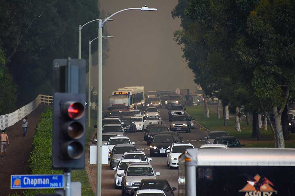 Kemacetan terjadi saat warga berbondong-bondong meninggalkan rumah mereka untuk mengungsi di Orange, California. Terlihat asap hitam pekat akibat kebakaran hutan di latar belakang. AFP/Robyn Beck