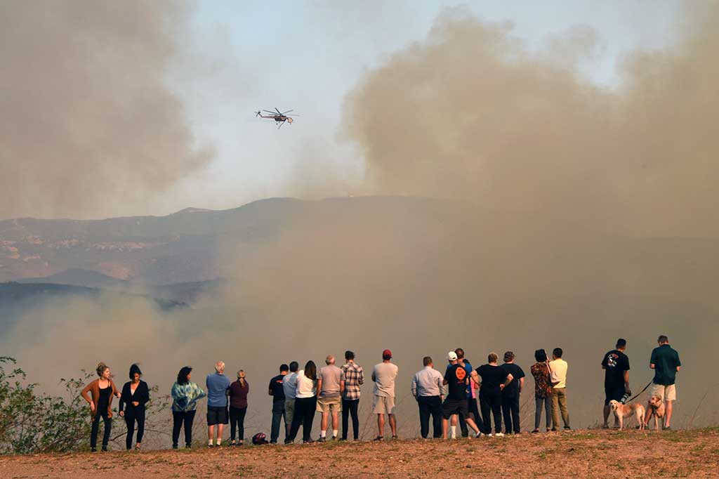 Warga melihat dari kejauhan sebuah helikopter yang mengangkut air untuk memadamkan kebakaran di Orange, California. AFP/Robyn Beck