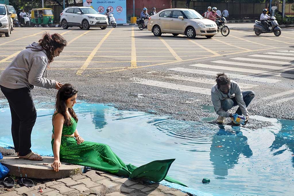 Seorang model dengan berbakaian seperti putri duyung ambil bagian dalam seni instalasi seniman Baadal Nanjundawsamy, Jumat 13/10/2017). Hal ini untuk memprotes banyaknya jalan berlubang di Bangalore.