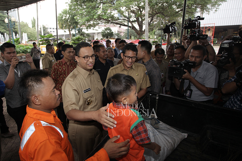 Setiba di halaman Balai Kota, Anies dan Sandi menyapa petugas kebersihan yang sedang membersihkan halaman dan membawa anak.