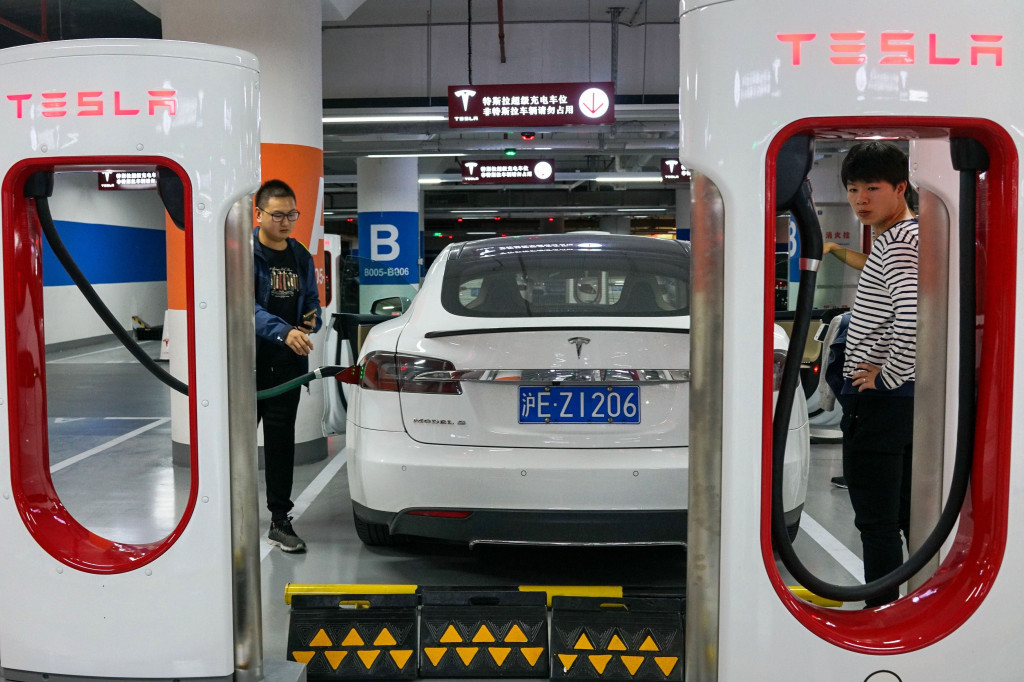 Dua pria mengisi listrik mobilnya Tesla-nya di stasiun pengisian listrik milik Tesla di basement parkir sebuah pusat perbelanjaan di Shanghai. 
