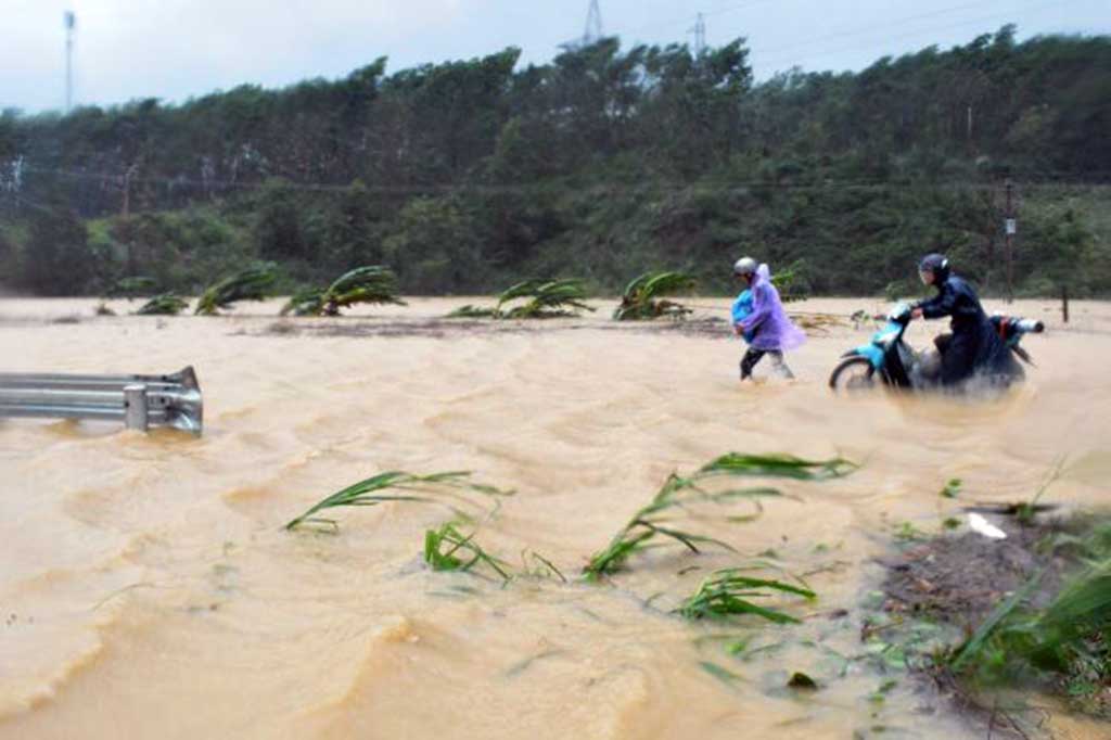 Pengendara motor nekat menerobos jalanan yang digenangi banjir yang dibawa topan Damrey di Provinsi Dak Lak, Vietnam, Sabtu (4/11/2017). 
