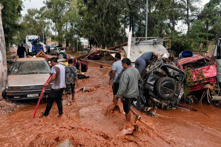 Warga melintas di jalanan yang dipenuhi lumpur dan puluhan kendaraan yang terseret banjir bandang di Mandra, barat laut Athena, Rabu, 15 November 2017 waktu setempat.