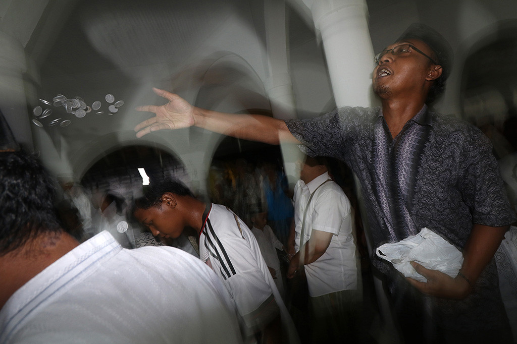 Seorang jamaah melemparkan koin untuk diperebutkan oleh jamaah lain di masjid Jami Jamsaren, Kota Kediri, Jawa Timur, Kamis (30/11) malam. Tradisi lempar uang logam yang turun temurun tersebut merupakan rangkaian acara perayaan Maulid Nabi Muhammad SAW sekaligus sebagai sarana syiar agama Islam. ANTARA/Prasetia Fauzani