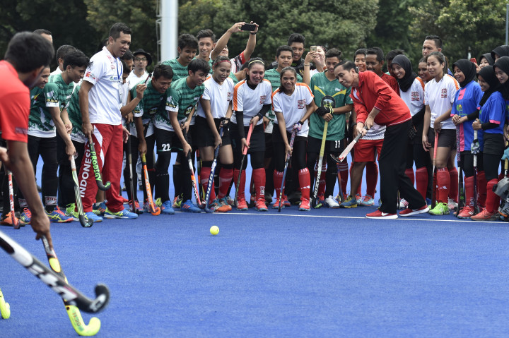 Mengenakan jaket merah, celana training hitam, dan sepatu merah, dia memukul bola hoki dan membaur dengan para atlet.