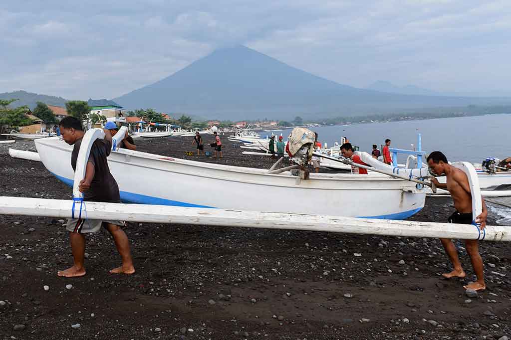 Nelayan mengangkat perahu saat mendarat di Pantai Amed dengan latar belakang Gunung Agung, di Karangasem, Bali, Selasa, 5 Desember 2017. ANTARA/Hafidz Mubarak A