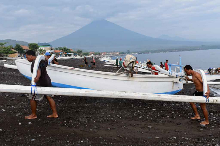 Nelayan mengangkat perahu saat mendarat di Pantai Amed dengan latar belakang Gunung Agung, di Karangasem, Bali, Selasa, 5 Desember 2017. ANTARA/Hafidz Mubarak A