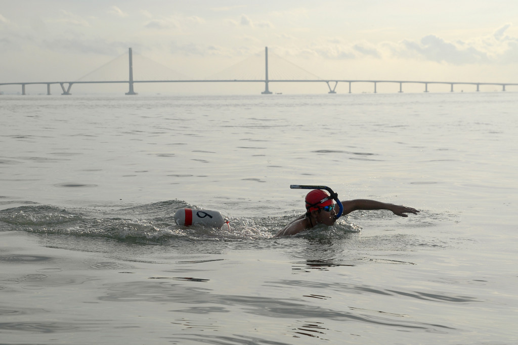 Seorang perenang melintas di samping Jembatan Suramadu (Surabaya-Madura).