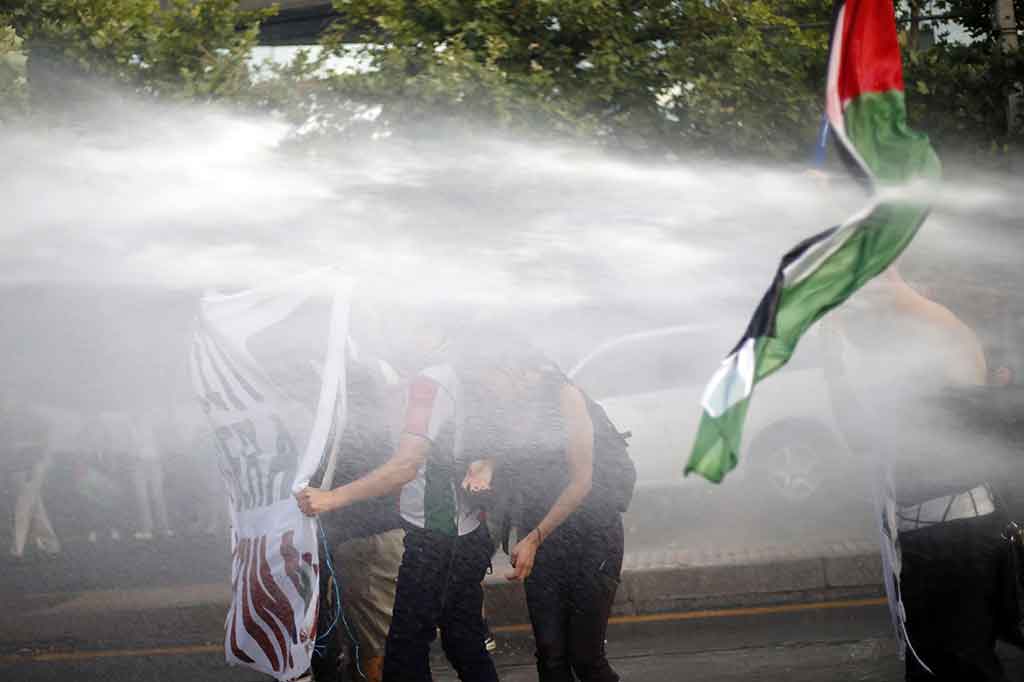 Para pengunjuk rasa berusaha bertahan dari semprotan air yang ditembakkan dari mobil water canon.