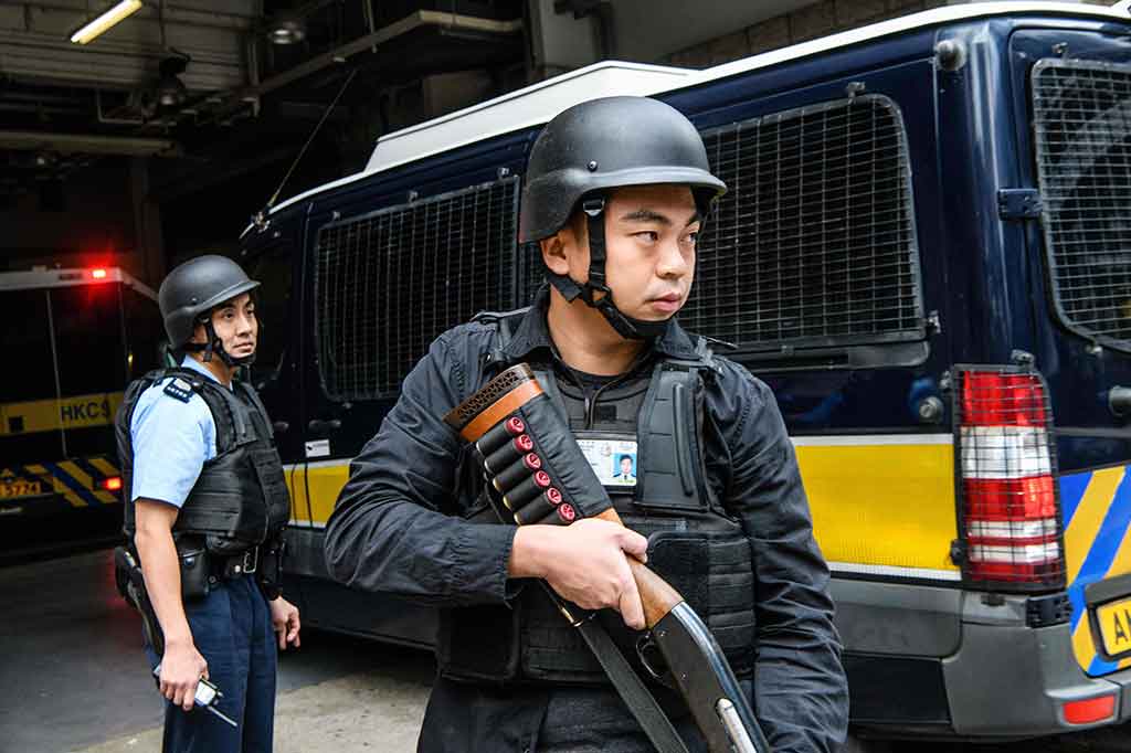 Petugas polisi dengan bersenjata lengkap berjaga di samping bus tahanan yang membawa bankir Inggris Rurik Jutting saat tiba di Pengadilan Tinggi di Hong Kong, Selasa, 12 Desember 2017.