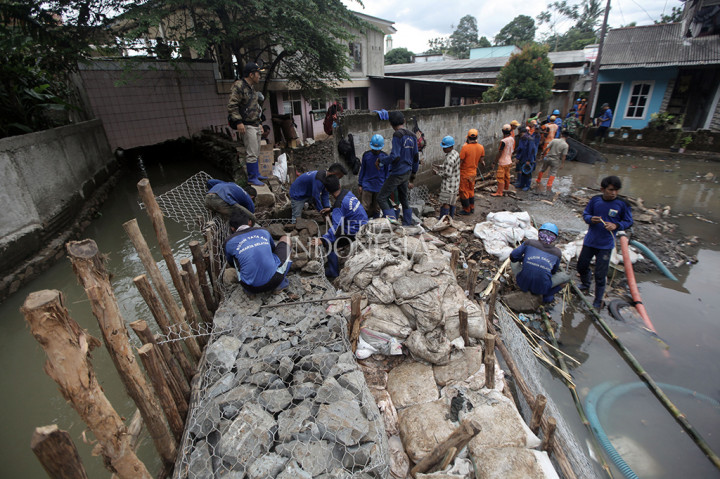 Petugas gotong royong membawa batu untuk pembangunan tanggul. Ada juga petugas yang membersihkan TK dekat tanggul yang terdampak banjir. 