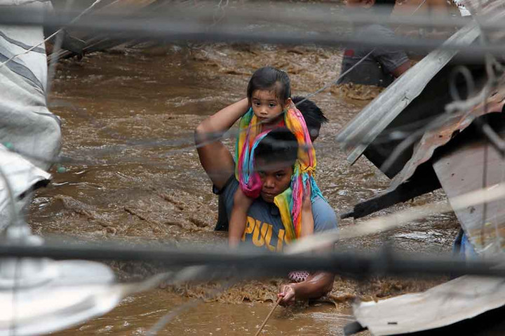 Seorang anggota polisi mengevakuasi seorang gadis cilik melintasi jalanan yang digenangi banjir di Kota Cagayan, Jumat, 22 Desember 2017. 
