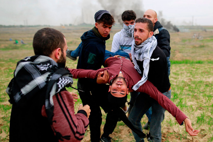 Pemuda Palestina mengangkat rekan mereka yang cedera selama bentrokan dengan tentara Israel di Kota Gaza. AFP/Mohammed Abed