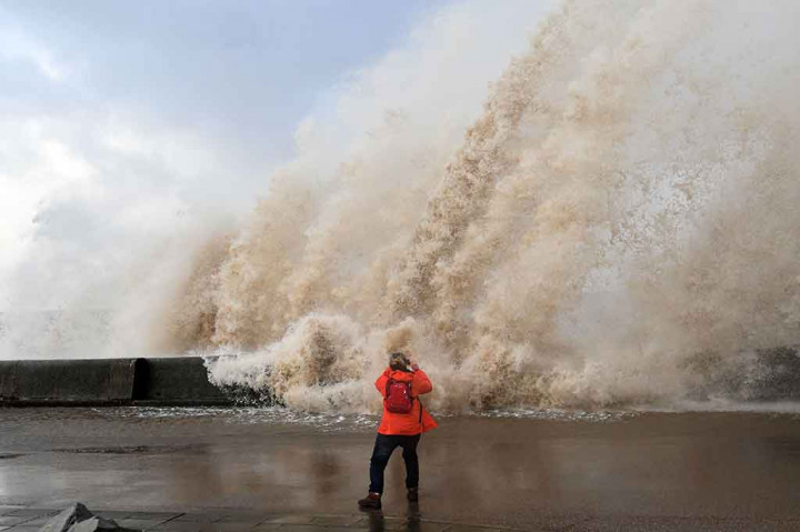 Seorang pengunjung mengambil gambar saat gelombang tinggi menghantam dinding beton di sepanjang pantai di New Brighton, Inggris. AFP/Paul Ellis
