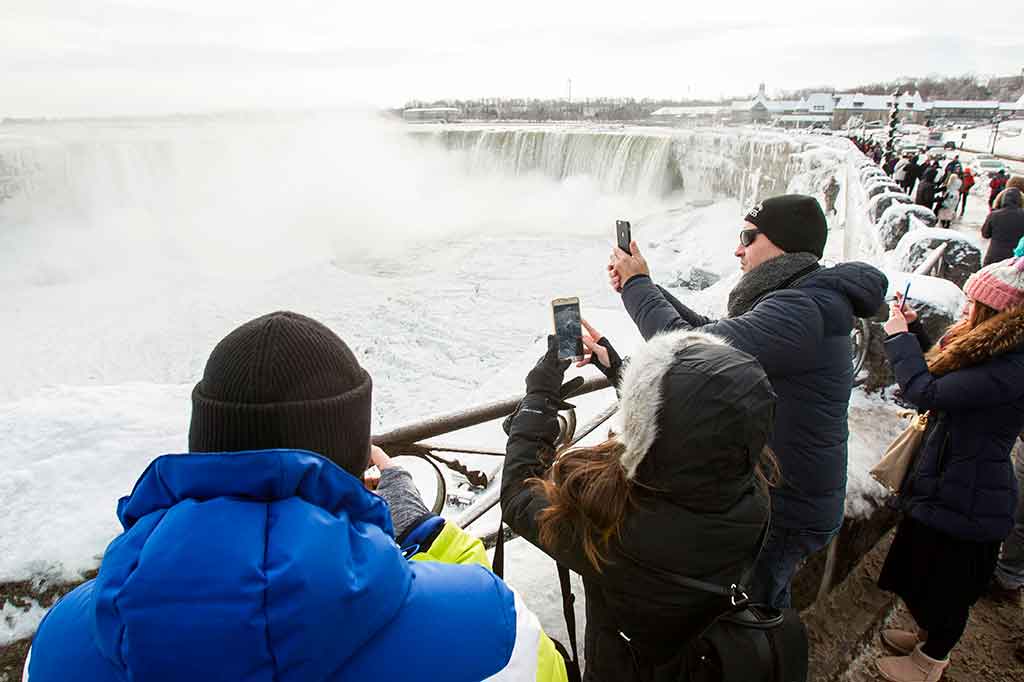Para turis mengabadikan pemandangan langka membekunya air terjun Niagara dengan ponsel mereka.