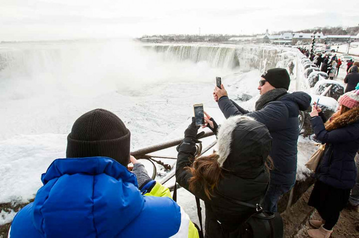 Para turis mengabadikan pemandangan langka membekunya air terjun Niagara dengan ponsel mereka.