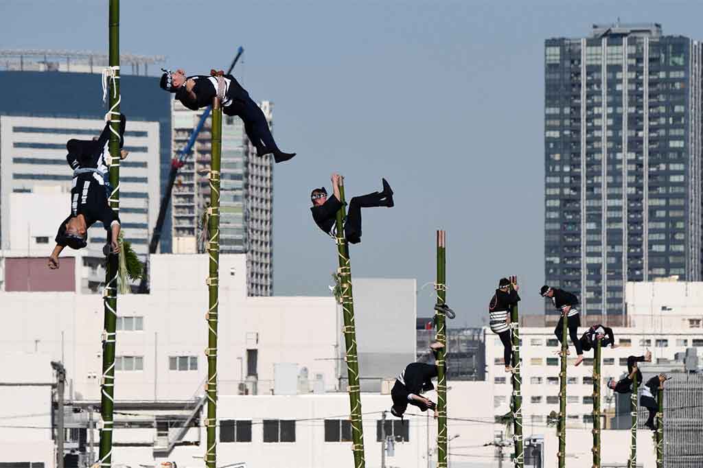 Tanpa mengenakan alat keselamatan mereka menunjukkan kemampuan keseimbangan di puncak tangga bambu yang didirikan rekan-rekan mereka secara manual.