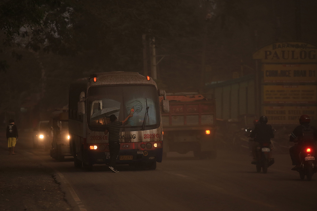 Seorang pengendara membersihkan kaca mobil dari abu vulkanik Gunung Mayon.