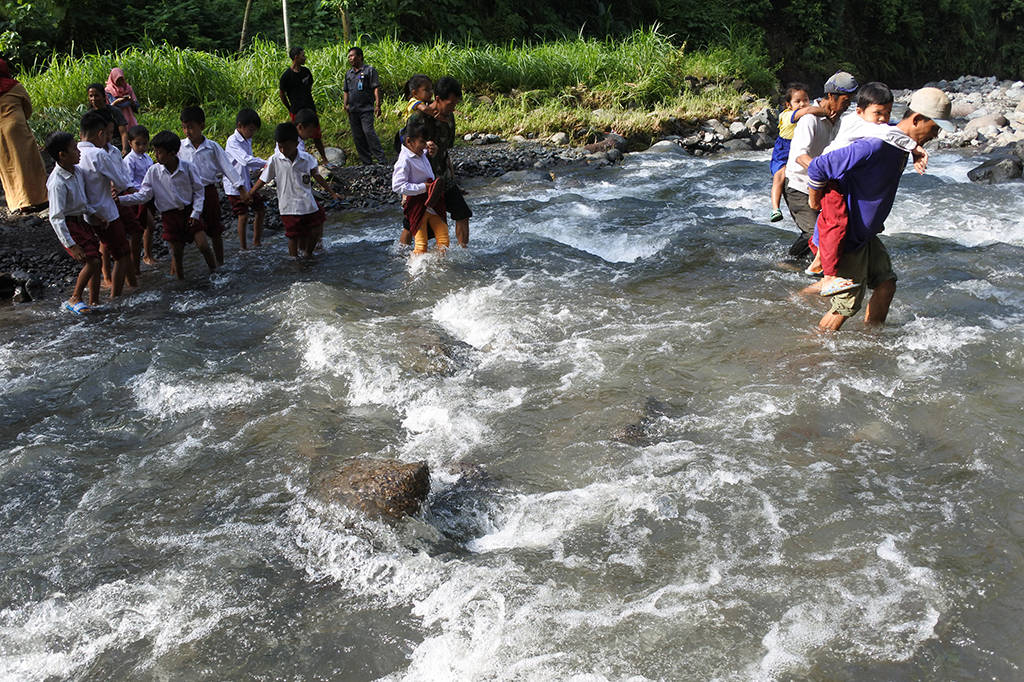 Siswa SDN 1 Campoan dibantu guru dan warga menyeberangi sungai di Desa Campoan, Mlandingan, Situbondo, Jawa Timur, Selasa, 30 Januari 2018. 