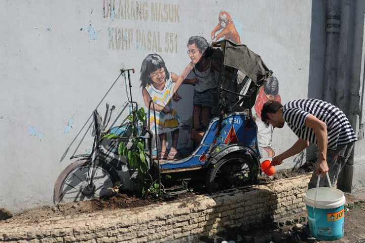 Pelukis jalanan dunia Ernest Zacharevic, menyiram tanaman di dekat mural yang digabungkan dengan miniatur becak motor karyanya di Jalan Perdana, Medan, pada 1 Maret 2017 lalu.
