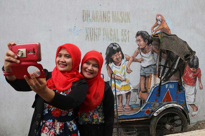 Dua perempuan berfoto dengan latar belakang mural yang digabung miniatur becak yang masih lengkap pada 22 Februari 2017 lalu. 