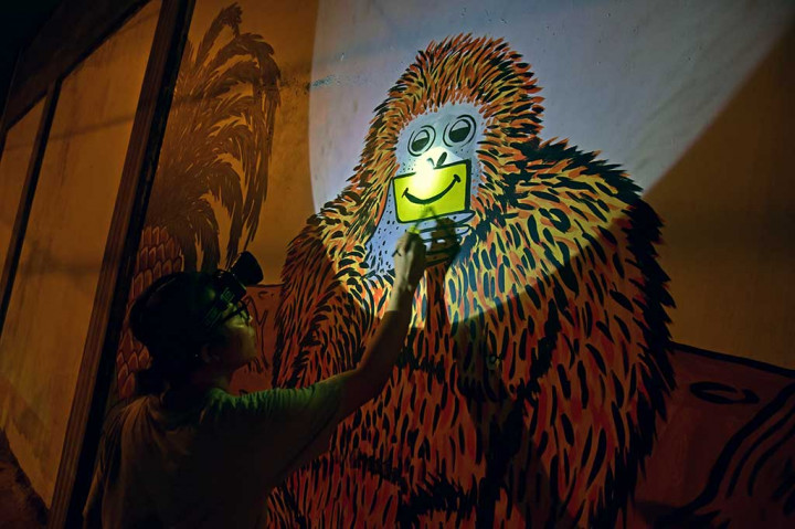 Seorang kartunis menyelesaikan mural bertema lingkungan berjudul 'Fake Smile' dengan bantuan senter kepala dan lampu motor saat peringatan 'Earth Hour', di Kota Pekanbaru, Riau, Sabtu 24 Maret 2018. ANTARA/FB Anggoro