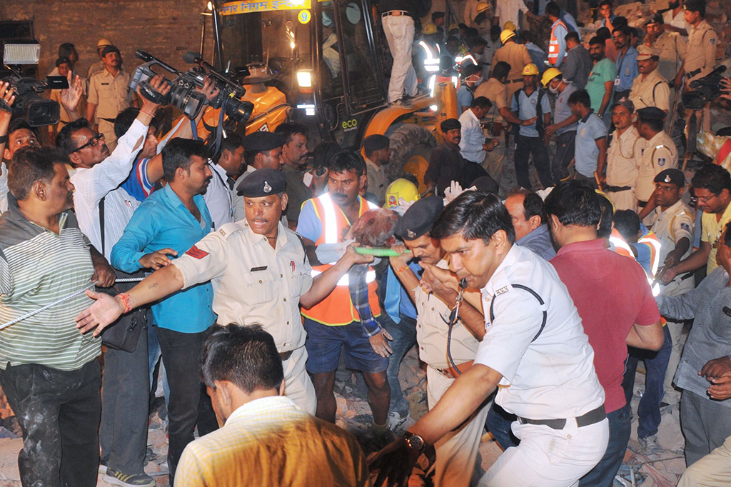 Petugas bahu membahu mengangkat reruntuhan bangunan secara manual untuk mencari para korban. Gedung yang ambruk itu digunakan sebagai tempat tinggal dan berada di tengah permukiman padat penduduk.