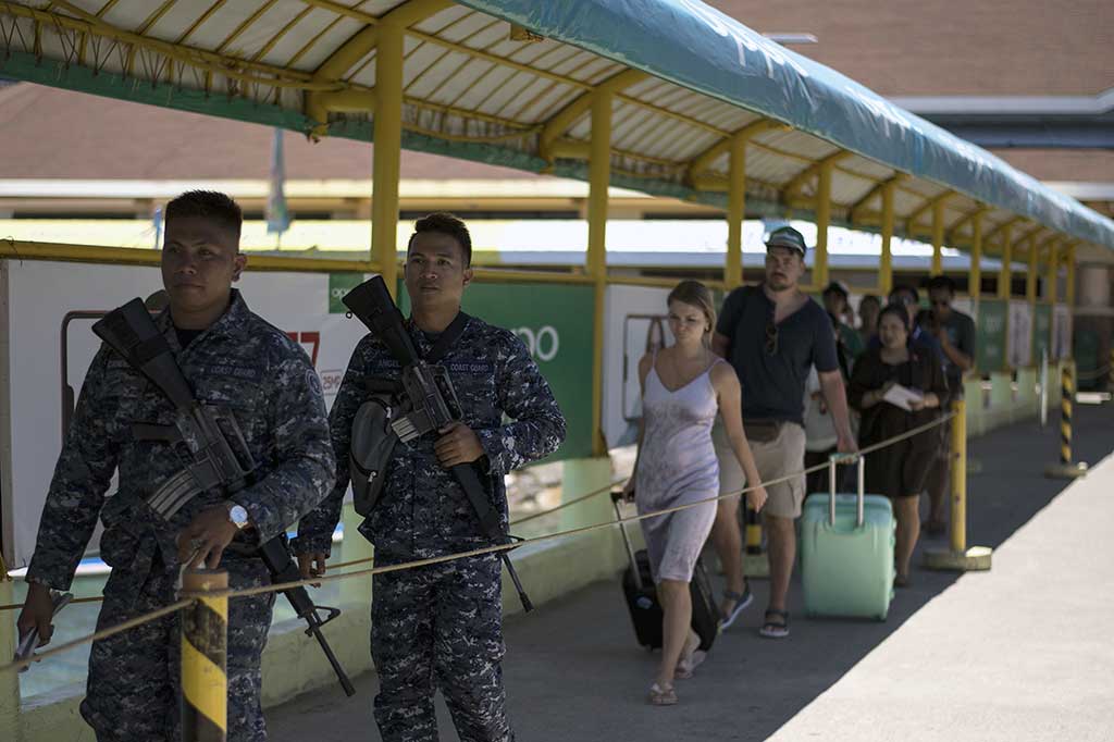 Aparat keamanan dengan senjata api berpatroli di antara wisatawan yang akan meninggalkan Pulau Boracay, Filipina, Selasa, 24 April 2018. Pulau Boracay akan ditutup untuk wisatawan selama enam bulan ke depan karena tercemar limbah.