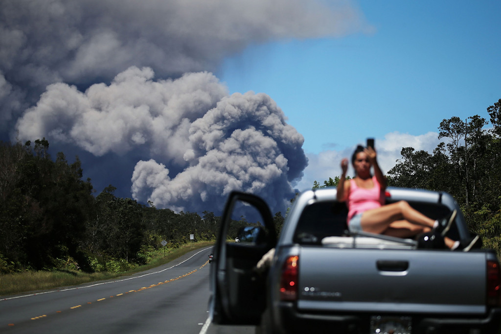 Sambil bersantai, seorang warga mengabadikan letusan gunung. 