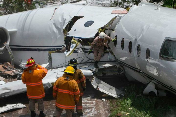 Petugas memeriksa badan pesawat yang terbelah untuk mencari penumpang dan awak pesawat yang terjebak di dalamnya.