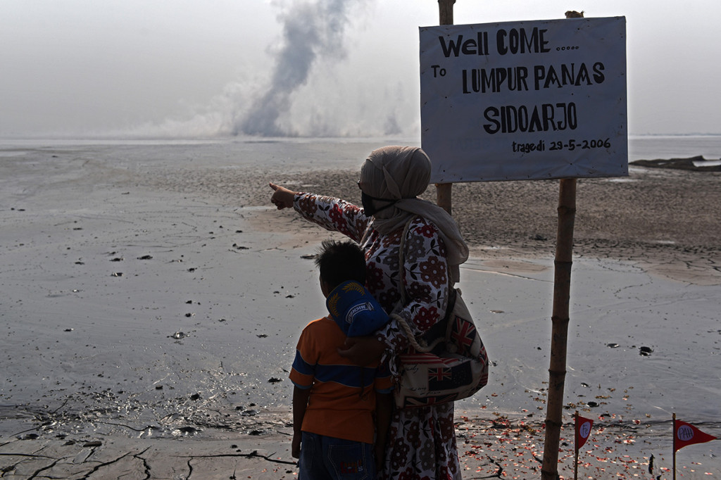 Seorang ibu bersama anaknya korban lumpur Lapindo menunjuk pusat semburan dari titik 25 tanggul penahan lumpur Lapindo saat aksi memperingati 12 tahun semburan lumpur Lapindo di Porong, Sidoarjo, Jawa Timur.
