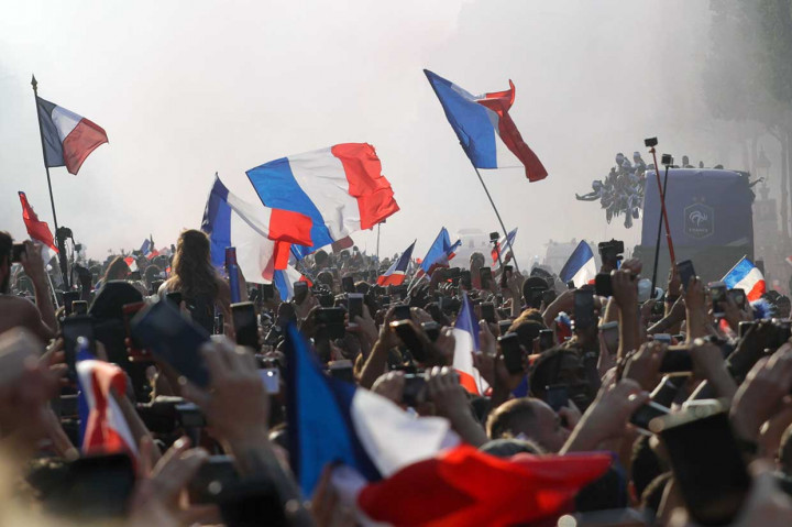 Ribuan warga bersuka cita menyambut Timnas Prancis sambil meneriakkan 'We Are The Champions', sementara para pemain mengabadikan momen tersebut dengan ponsel mereka.