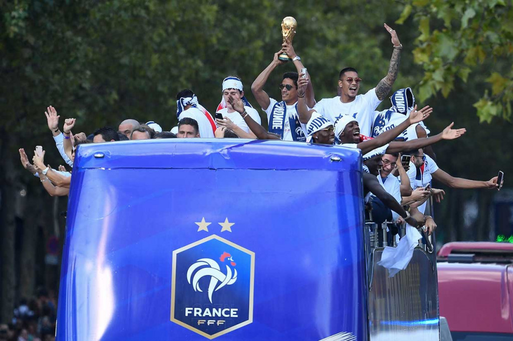 Raphael Varane mengangkat trofi Jules Rimet, sementara rekan-rekannya melambaikan tangan sembari merekam momen penyambutan kepada mereka.