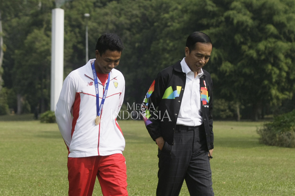 Jokowi tampak mengenakan jaket Asian Games, sedangkan Zohri mengenakan jaket putih dan mengalungkan medali emas.