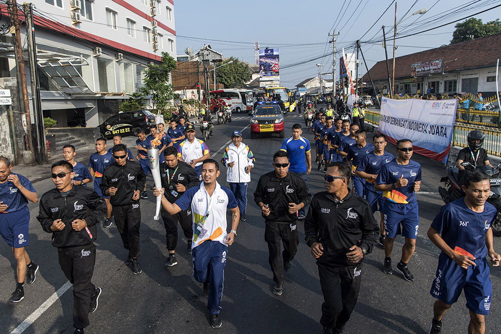Penyanyi Rio Febrian (tengah) membawa obor saat prosesi Torch Relay Asian Games 2018 melintasi kawasan Pasar Kembang, Yogyakarta, DI Yogyakarta.
