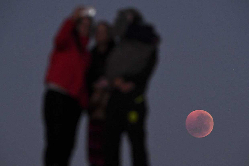 Warga berswafoto dengan latar belakang gerhana bulan total di Melbourne, Australia. AFP Photo/William West