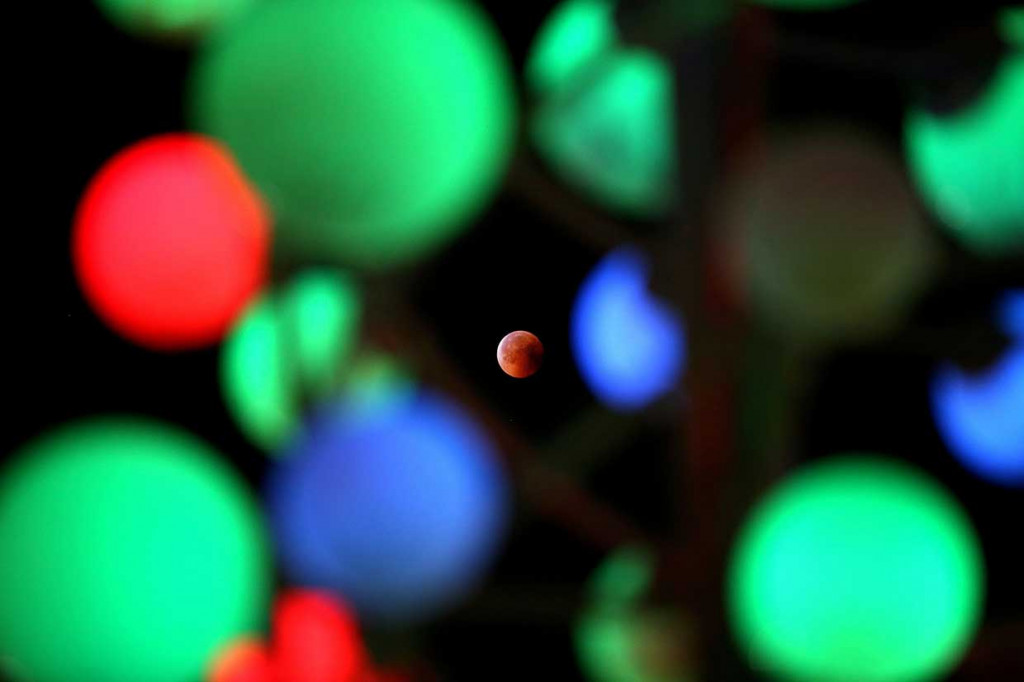 Gerhana bulan total atau micro blood moon terlihat di antara lampu berwarna-warni di Kuwait. AFP Photo/Yasser Al-Zayyat