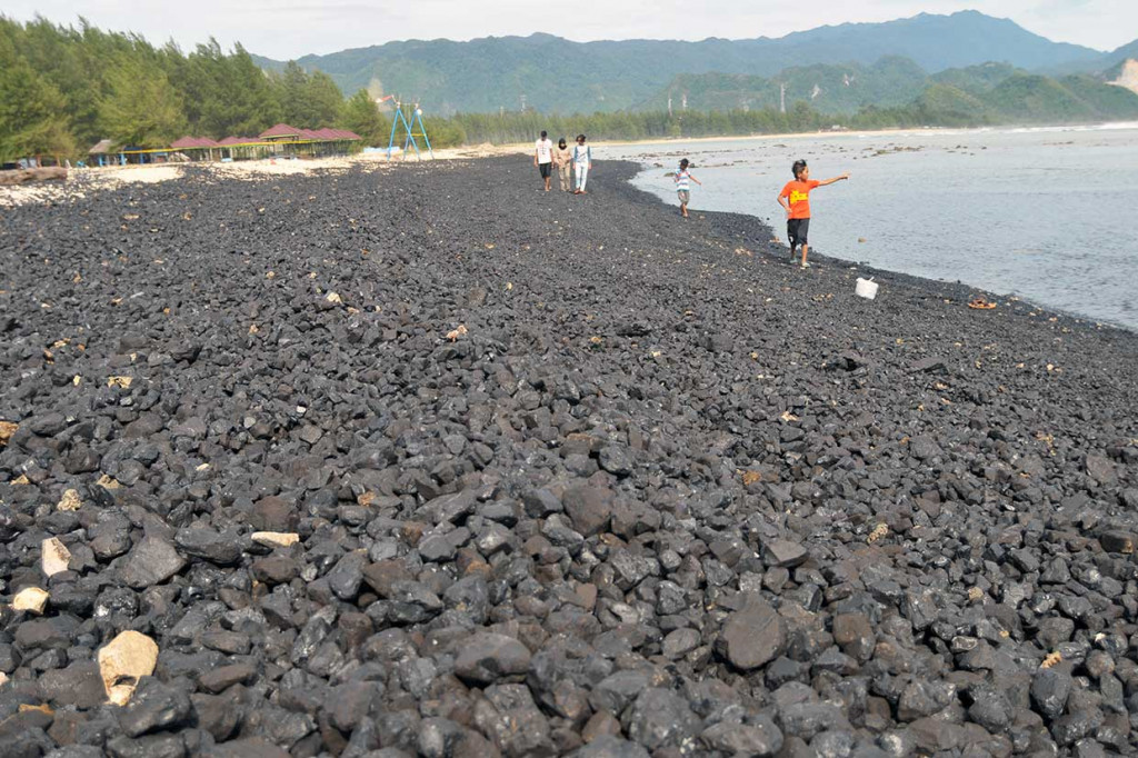 Pengunjung bermain di pantai yang sebagian tertutup batu bara tumpahan dari kapal tongkang yang kandas di peraian Ujung Kareng, Kecamatan Lhoknga, Kabupaten Aceh Besar, Aceh, Selasa, 31 Juli 2018. 