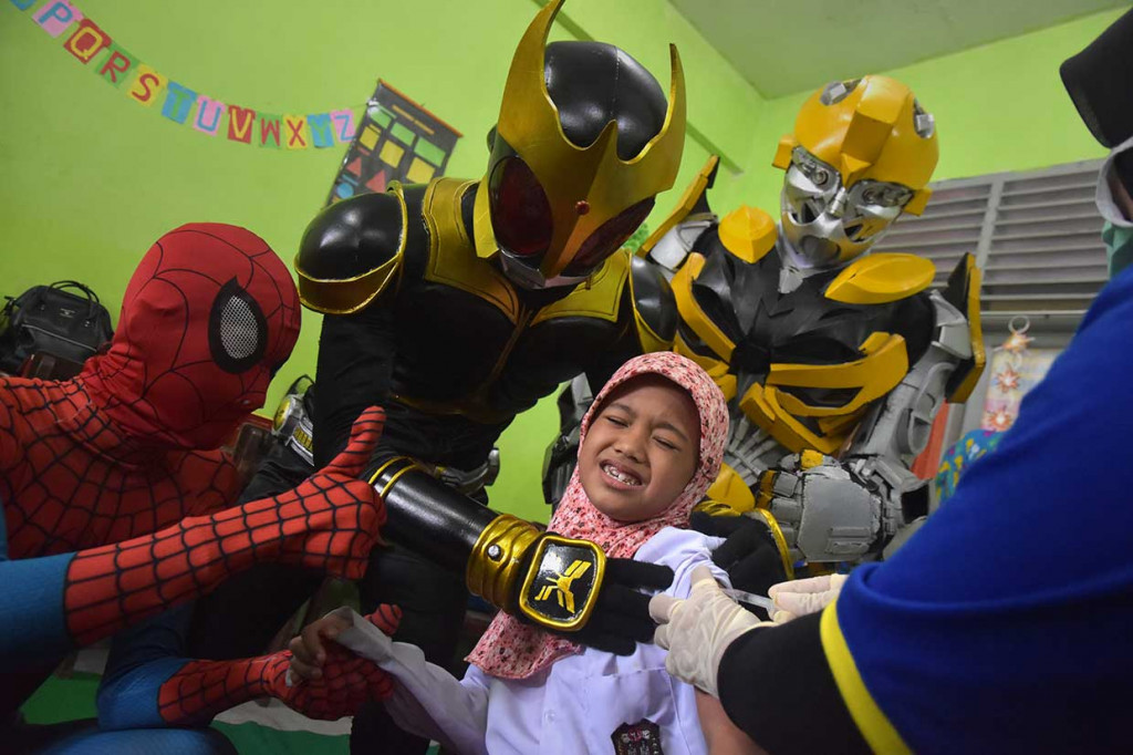Seorang anak ditemani komunitas kostum superhero Spiderman, Kamen Raider, dan Bumblebee saat imunisasi campak (measles) dan rubella (MR) di SDN 2 Kota Pekanbaru, Riau, Rabu, 1 Agustus 2018. Antara Foto/FB Anggoro