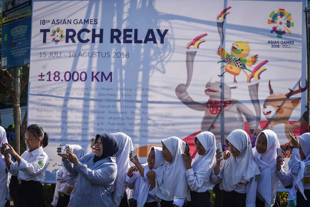 Warga bersama pelajar memotret menggunakan ponsel mereka saat kirab obor Asian Games di Bandung, Jawa Barat, Sabtu, 11 Agustus 2018.