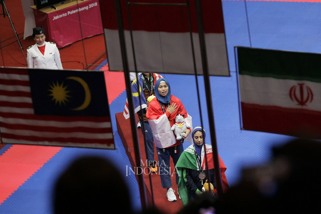 Atlet Taekwondo Indonesia Defia Rosmaniar (tengah) menyanyikan lagu kebangsaan Indonesia Raya saat penyerahan medali setelah mengalahkan atlet taekwondo Iran, Marjan Salahshouri pada nomor poomsae individu putri di Plenary Hall Jakarta Convention Centre. MI/Ramdani
