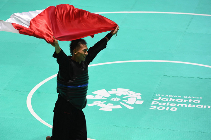 Pesilat Indonesia Iqbal Chandra Pratama membentangkan bendera merah putih usai mengalahkan pesilat Vietnam Ngoc Toan Nguyen dan meraih medali emas dalam babak final Kelas D Putra Asian Games 2018 di Padepokan Pencak Silat Taman Mini Indonesia Indah (TMII), Jakarta.