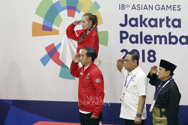 Presiden Joko Widodo bersama Ketua PB IPSI Prabowo Subianto dan Chief de Mission tim Indonesia di Asian Games sekaligus Menpan RB Komjen Syafruddin memberi hormat dan menyanyikan Indonesia Raya ketika memberikan medali emas kepada pesilat Indonesia Wita Wewey. MI/Rommy Pujianto
