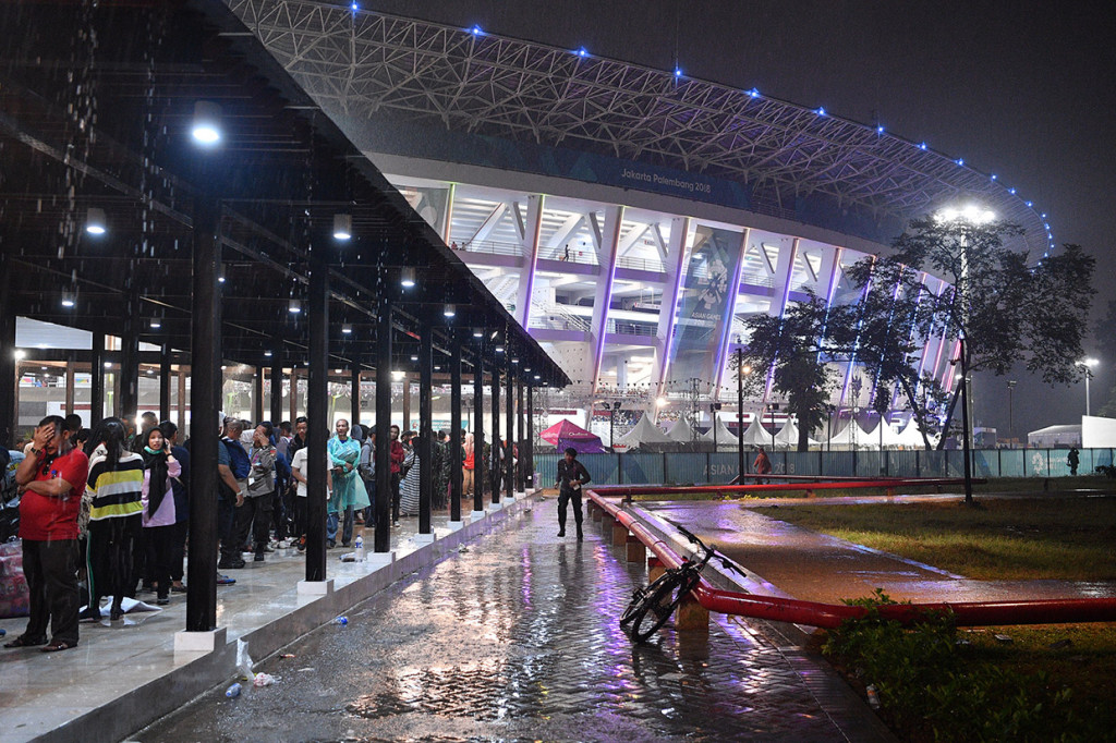 Warga berteduh saat hujan mengguyur di sela Upacara Penutupan Asian Games ke-18 Tahun 2018 di kawasan Stadion Utama GBK, Senayan, Jakarta.  Antara Foto/INASGOC/Sigid Kurniawan