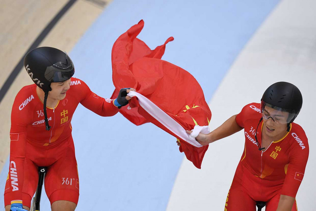 Atlet balap sepeda Tiongkok Chenlu Qin (kanan) dan Liang Guo membawa bendera negaranya setelah berhasil merebut emas Final Putra Team Persuit. INASGOC/Antara Foto/Mohammad Ayudha