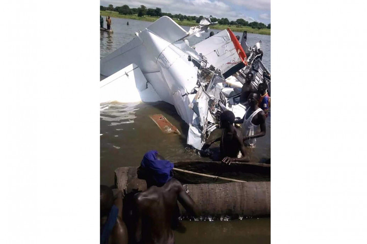 Gambar menunjukkan reruntuhan bengkok pesawat yang tenggelam dalam air. Nelayan lokal menggunakan kano untuk membantu upaya penyelamatan dan pengambilan.