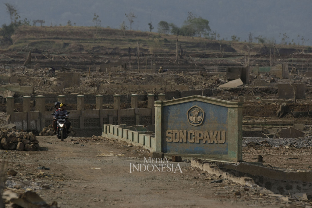 Warga melintas diantara puing sisa bangunan sekolah yang dulunya merupakan wilayah Desa Cipaku, Kecamatan Darmaraja, Kabupaten Sumedang, Jawa Barat.