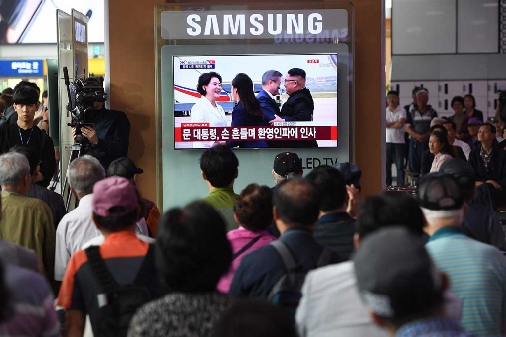 Warga melihat siaran televisi di sebuah stasiun kereta api di Seoul, Selasa, 18 September, yang menunjukkan rekaman langsung tentang kedatangan Presiden Korea Selatan Moon Jae-in di Bandara Pyongyang dan disambut pelukan Pemimpin Korut Kim Jong Un. 